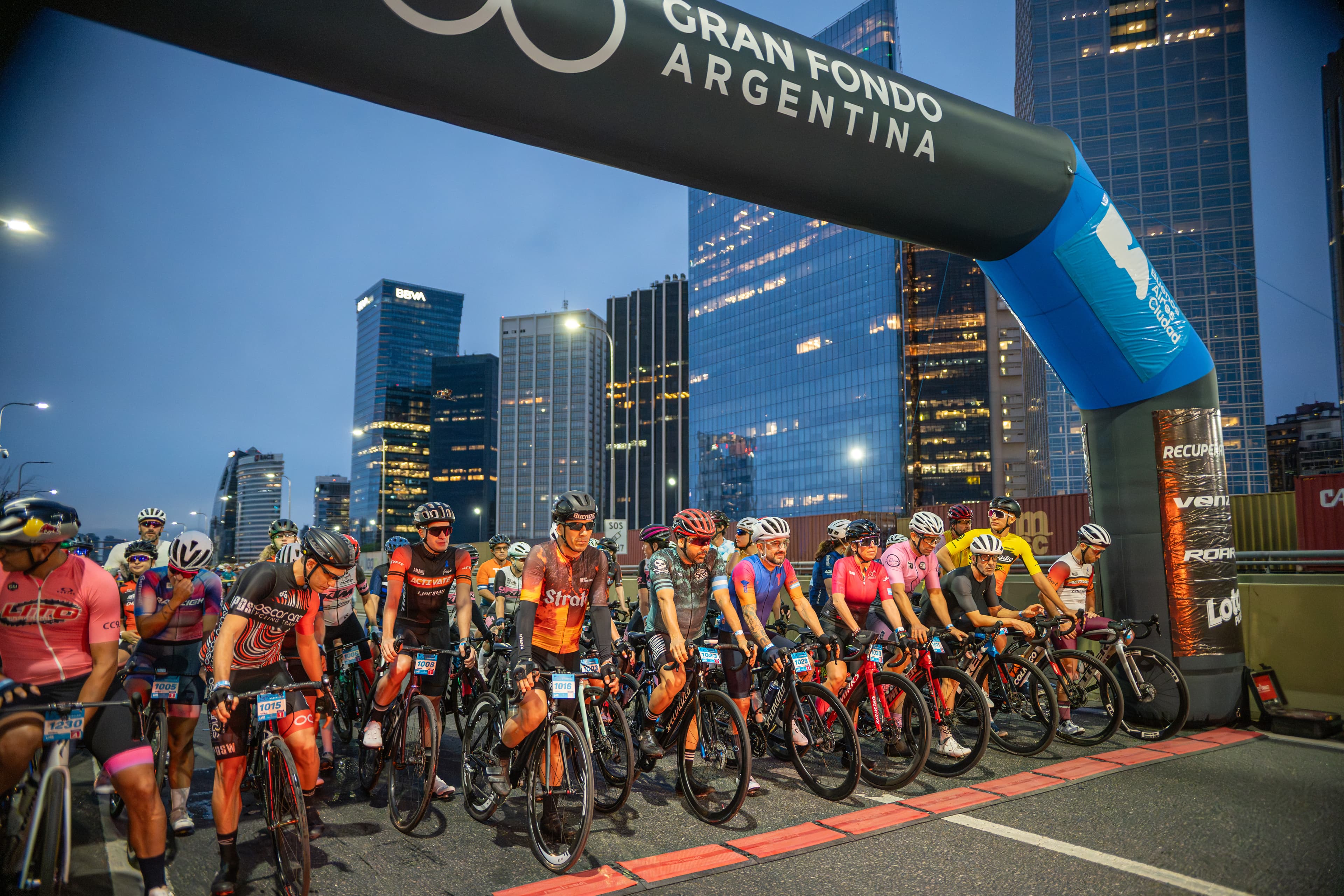 Cyclists lined up at dawn under the Gran Fondo Argentina start arch, with the Buenos Aires skyline behind them