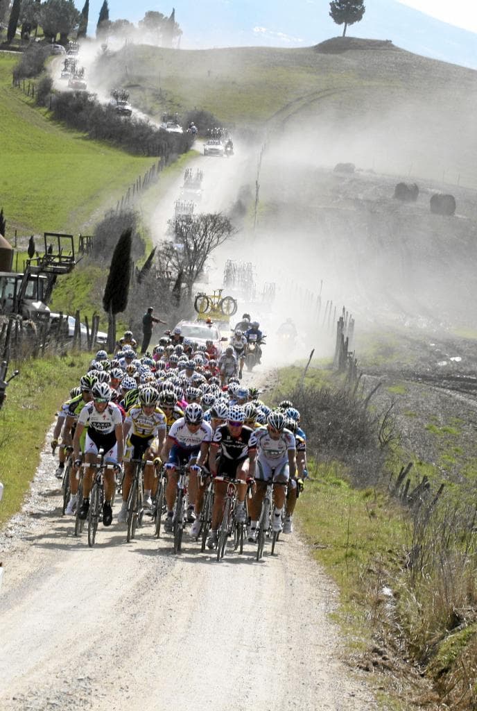 Cyclists riding the white gravel roads of Tuscany during the Strade Bianche Gran Fondo with Siena in the background